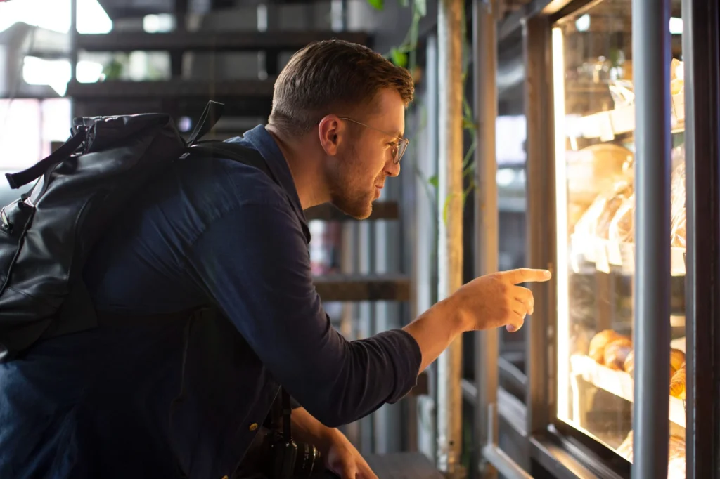 A man with a backpack selecting a snack from a well-lit vending machine in a modern setting